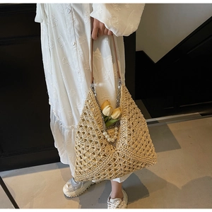 Dettaglio borsa tote in paglia intrecciata con tracolla in pelle e ciondolo di perle