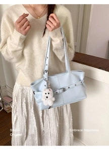 Light blue faux leather tote bag detail with white plush dog charm and buckle strap