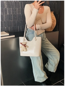 Fashionable cream PU leather tote bag with bear charm shown on model in minimalist setting