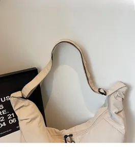 Detail view of beige nylon crescent bag with adjustable strap and black metal hardware