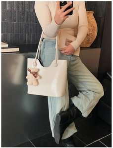 Close-up of cream leather tote bag with a cute bear plush charm and wavy top design