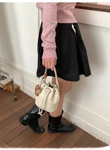 Detail of cream drawstring bucket bag with textured leather and brown woven charm
