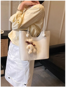 Close-up of cream faux leather tote bag with a wavy edge and cute plush bear charm
