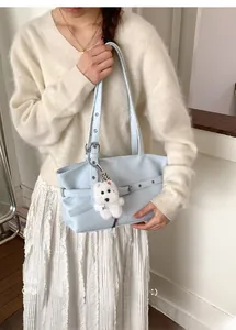 Detail of light blue leather tote bag with silver buckle and white plush dog charm