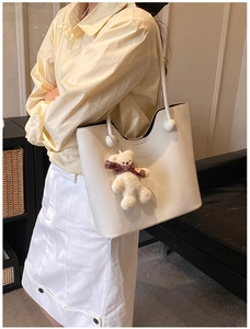 Close-up of white PU tote bag with unique spherical handle and cute teddy bear charm
