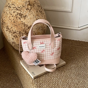 Pink checkered bucket handbag with heart charm and bow details shown in a cozy setting