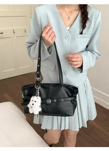 Close-up of black leather tote bag with silver buckle and white plush dog charm
