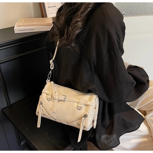Detail view of cream white biker-style crossbody bag with silver zippers on a model