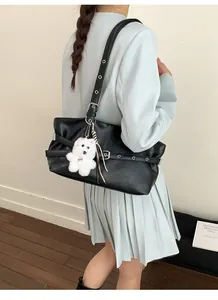 Minimalist black tote bag shown on shoulder with plush bear charm and sleek leather finish