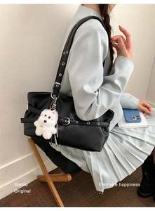 Detail of black leather tote bag with silver metal buckle and white puppy plush keychain