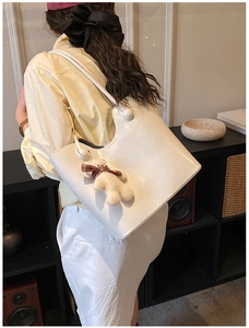 Detailed view of cream white patent leather shoulder bag with cute teddy bear charm pendant