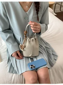 Close-up of cream drawstring bucket bag with wood pony charm on soft white background