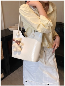 Detail of white glossy leather tote bag featuring a cute plush bear charm with scarf