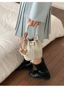Detail of cream drawstring bucket bag with a wooden rocking horse charm in a cozy indoor setting