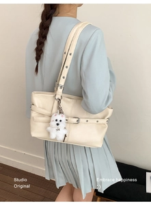 Detail of minimalist cream tote bag with silver eyelets and a white plush dog pendant