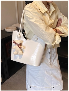 Detail of white glossy PU leather tote bag with a cute plush bear charm for daily wear