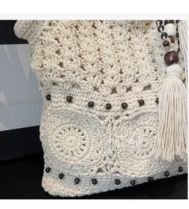 Close-up of beige crochet shoulder bag showing hollow patterns, wooden beads and tassels