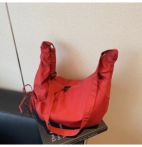 Red nylon crescent dumpling bag on a black book showing stylish pleated texture and strap