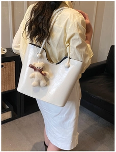 Detail view of large white patent leather tote bag with round buckle and plush bear charm