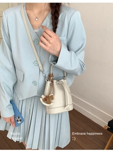 Lifestyle view of cream drawstring bucket bag with rocking horse charm and blue suit