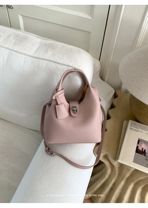Close-up of pink litchi grain leather bucket bag with silver twist lock on white sofa
