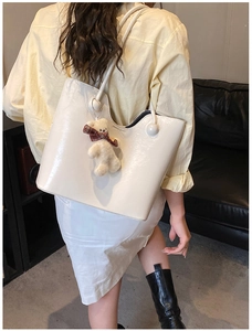 Detail view of white patent leather tote bag with wavy trim and cute teddy bear charm