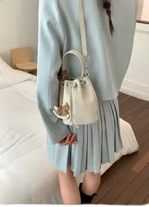 Rear view of a beige drawstring bucket bag shown on model in a light blue suit