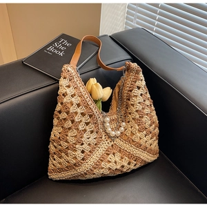 Dettaglio borsa tote in paglia intrecciata con manici in pelle e ciondolo di perle