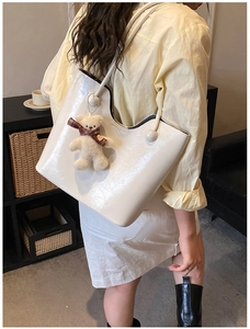 White glossy leather tote bag with a cute plush bear charm in a lifestyle home setting