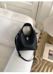 Close-up of black lychee grain leather bucket bag with silver metal buckle on a white sofa