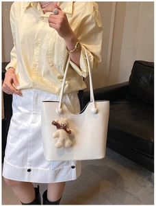 Close-up of a white leather tote bag featuring a cute teddy bear charm on the handle