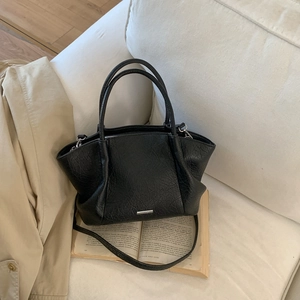 Détail de sac cabas noir vintage avec logo en métal sur un fond en tissu beige élégant