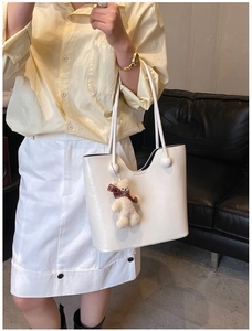 Detailed close-up of white glossy tote bag featuring a cute beige plush bear pendant