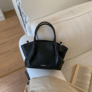 Sac fourre-tout noir chic en cuir craquelé posé sur un canapé blanc doux