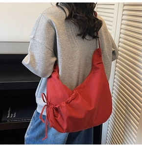 Detail view of red nylon crescent bag worn on shoulder showing drape and texture