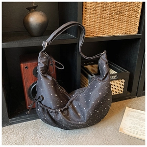 Close-up of black crescent bag with silver star prints and wide adjustable shoulder strap