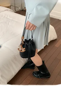Detail of black lychee leather bucket bag with drawstring and wooden horse charm decor