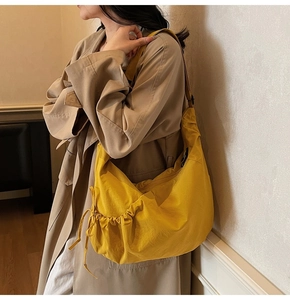 Detail view of yellow dumpling bag showing side drawstring texture and adjustable strap