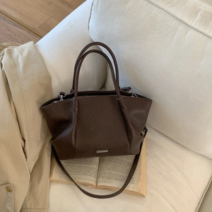 Détail du cabas marron foncé avec texture cuir rétro et logo argenté sur un canapé blanc