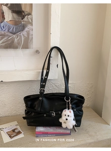 Close-up of black tote bag with metal buckle detail and a cute white puppy plush charm