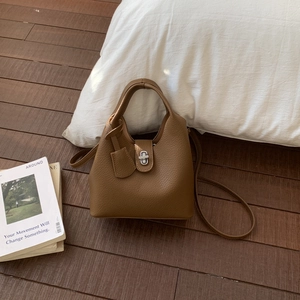 Brown lychee leather bucket bag with silver metal lock on a vintage wood background