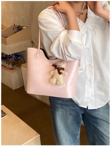 Detailed view of a pink glossy tote bag worn by a model with a cute white bear pendant