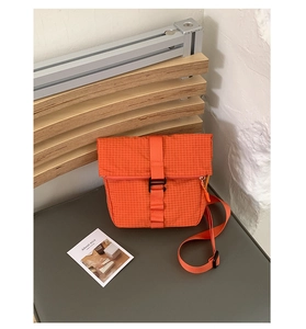 Détail du sac bandoulière orange à carreaux en nylon avec boucle noire et texture