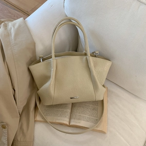 Détail du sac cabas en cuir plissé crème avec logo métallique sur un livre
