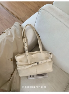 Detail view of cream-colored tote bag with adjustable straps on a white sofa scene