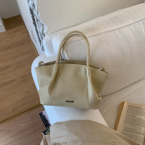 Détail du sac fourre-tout crème en cuir avec une plaque logo en métal argenté sur un canapé