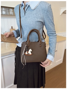 Dettaglio di una borsa in pelle marrone con doppi manici e un ciondolo decorativo a cavallino