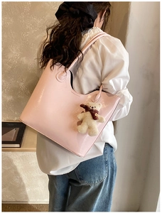 Detail view of a large pink tote bag with a plush bear charm on a model's shoulder