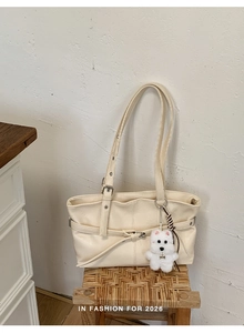 Detail of cream leather tote bag with stylish plush puppy and woven charms on a woven stool