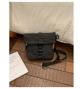 Détail du sac bandoulière imperméable à carreaux avec boucle de sécurité et étiquette orange